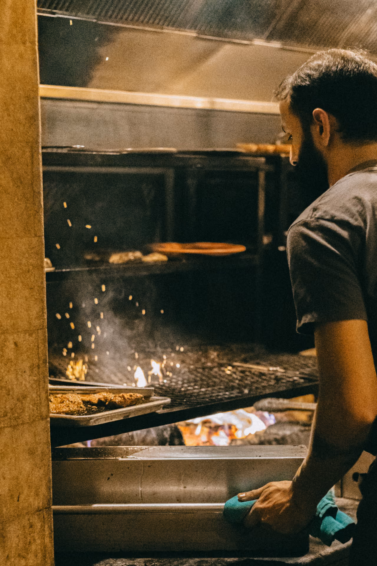 Cook working over a charcoal grill in a restaurant kitchen, photographed by Jasmine Tam